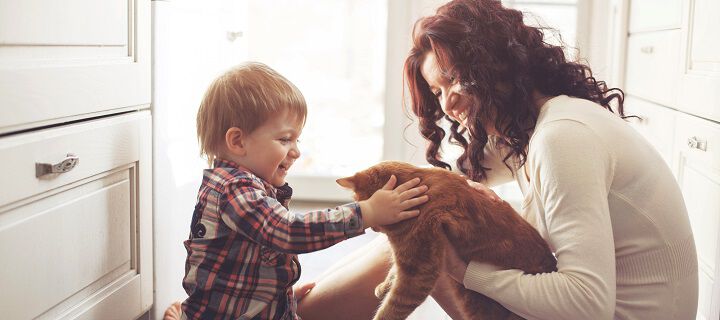 A woman and a child petting a dog on a kitchen floor.